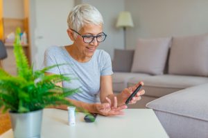 Happy mature woman with glucometer checking blood sugar level at home